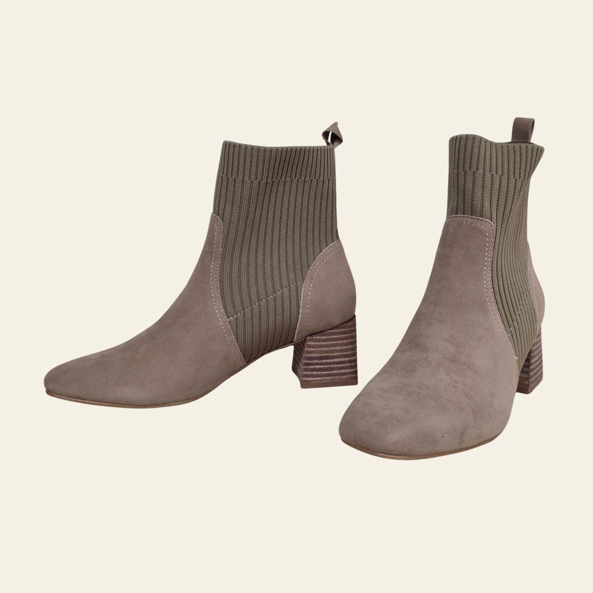 A pair of taupe suede ankle boots with ribbed knit socks, shown from the side and front angles against a solid cream background.