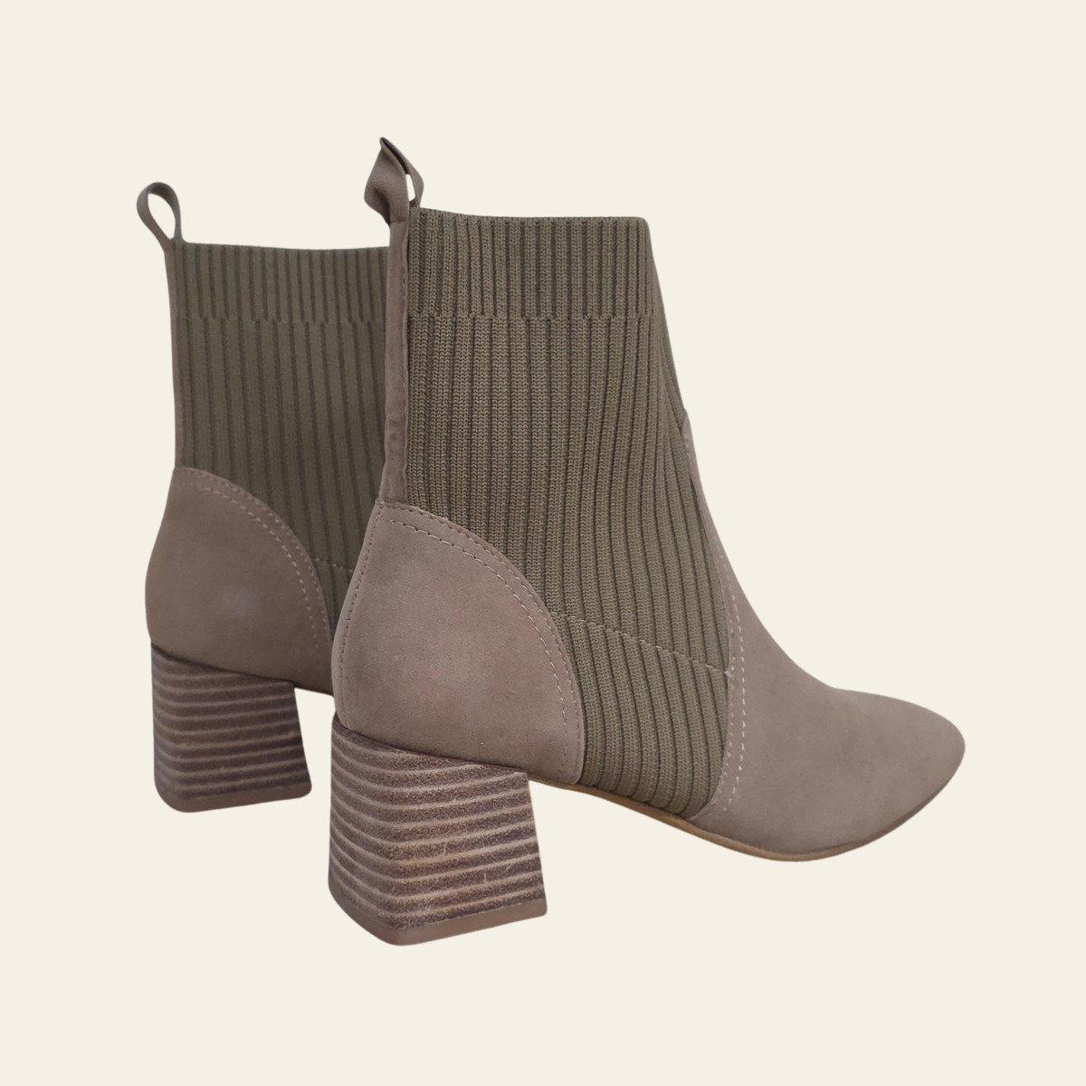 A pair of women's ankle boots in taupe, featuring a ribbed knit sock-style shaft and a stacked block heel, shown against a solid cream background.