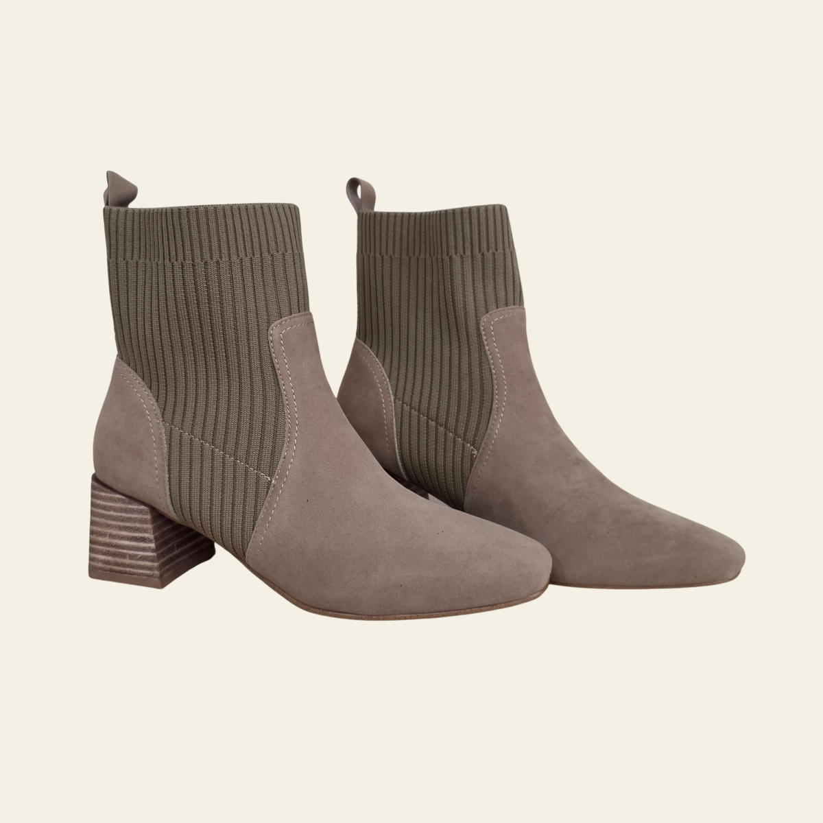 A pair of taupe suede ankle boots with ribbed knit socks, shown against a solid cream background.