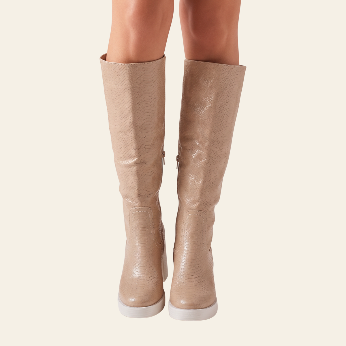 A pair of knee-high beige snakeskin-textured boots with white platform soles, shown on a model's legs against a light cream background.