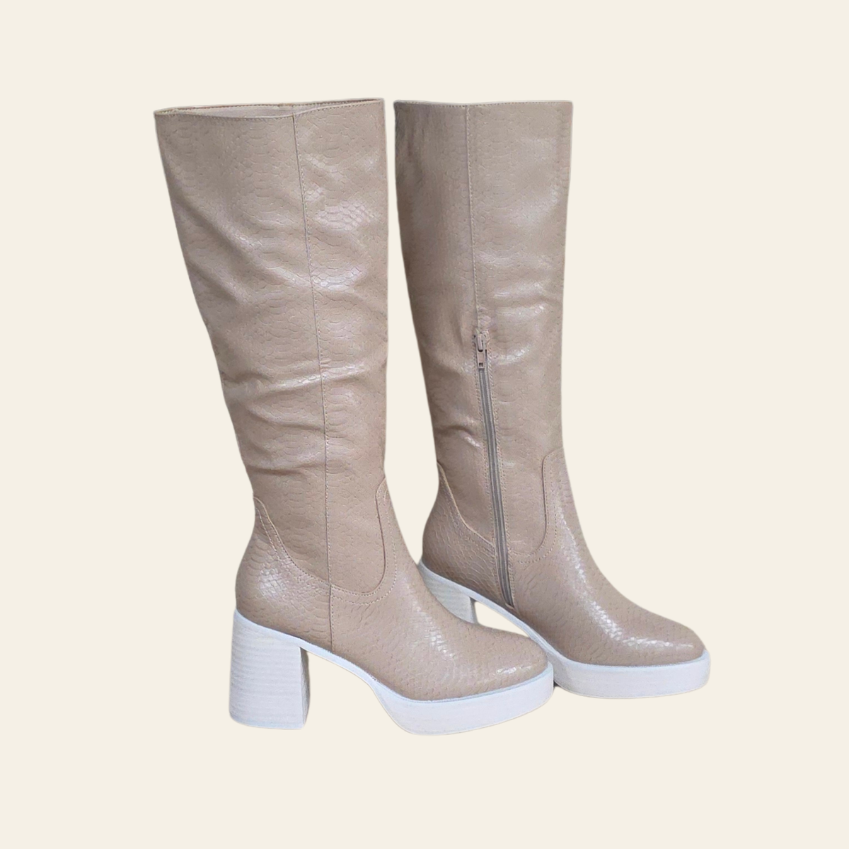 A pair of knee-high boots in a light beige faux-leather material with a subtle textured pattern, featuring a chunky white block heel and a silver zipper on the side, set against a solid cream background.