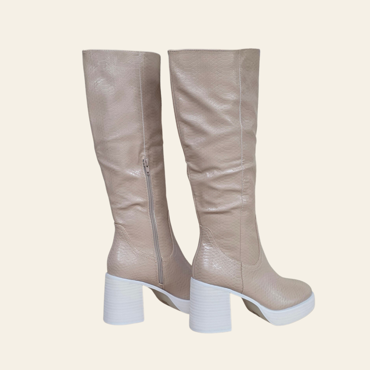A pair of knee-high boots in a textured light taupe leather with a white block heel and sole, shown from a side profile view against a solid cream background.