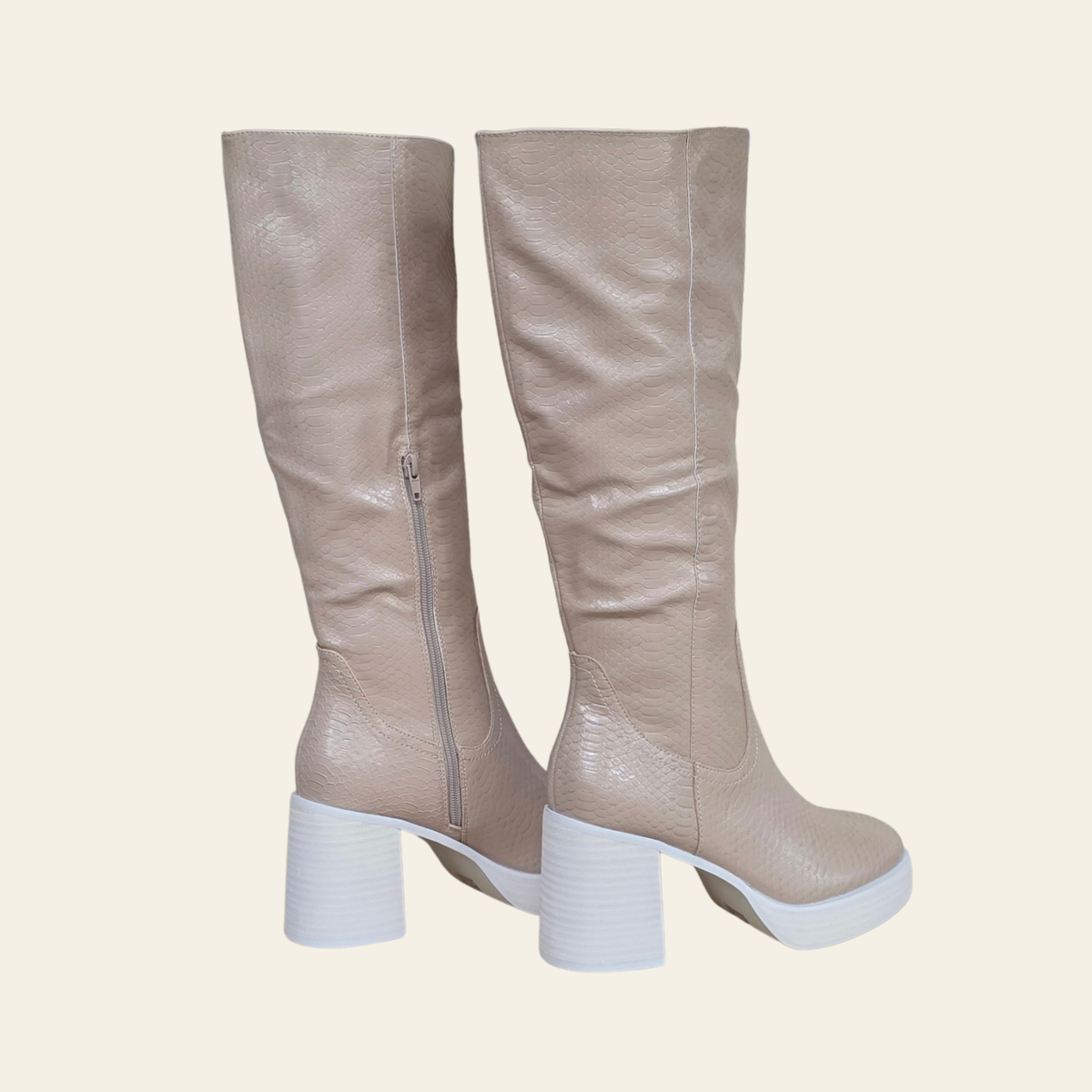 A pair of knee-high boots in a textured light beige faux leather, featuring a white block heel and sole, shown from a side profile view against a solid cream background.