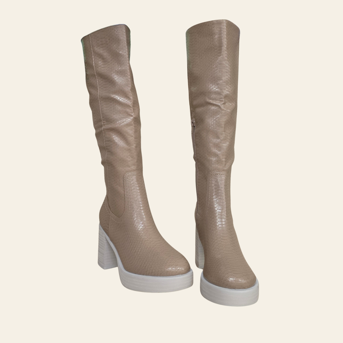 A pair of knee-high boots in a textured taupe-beige leather with chunky white platform soles and block heels, shown against a solid cream background.