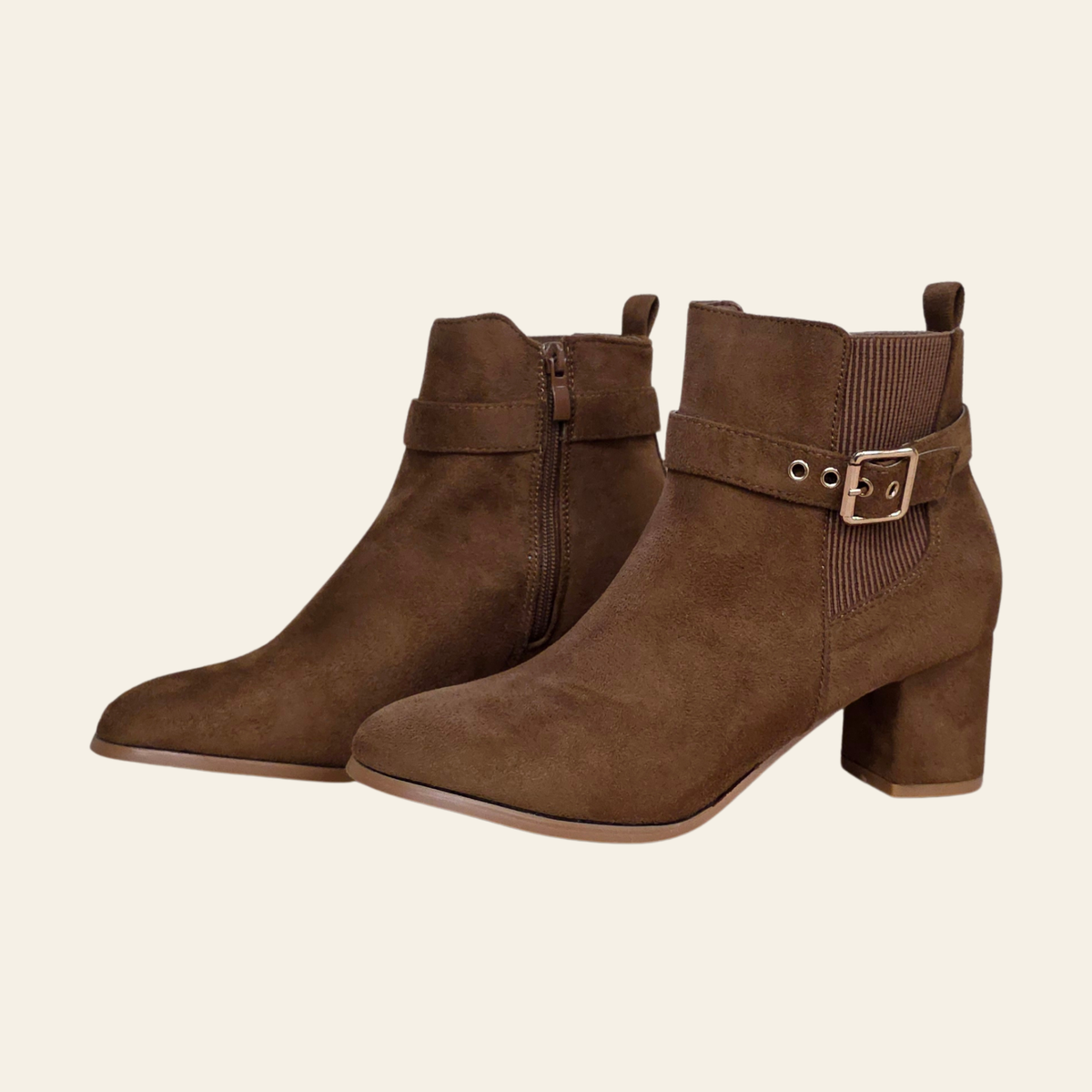 A pair of women's brown suede ankle boots with block heels, side zippers, and decorative buckle straps, shown against a solid light cream background.