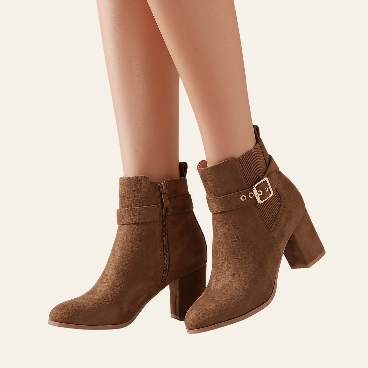 A pair of women's brown suede ankle boots with block heels, side zippers, and a decorative buckle strap, shown on a model's feet against a light cream background.