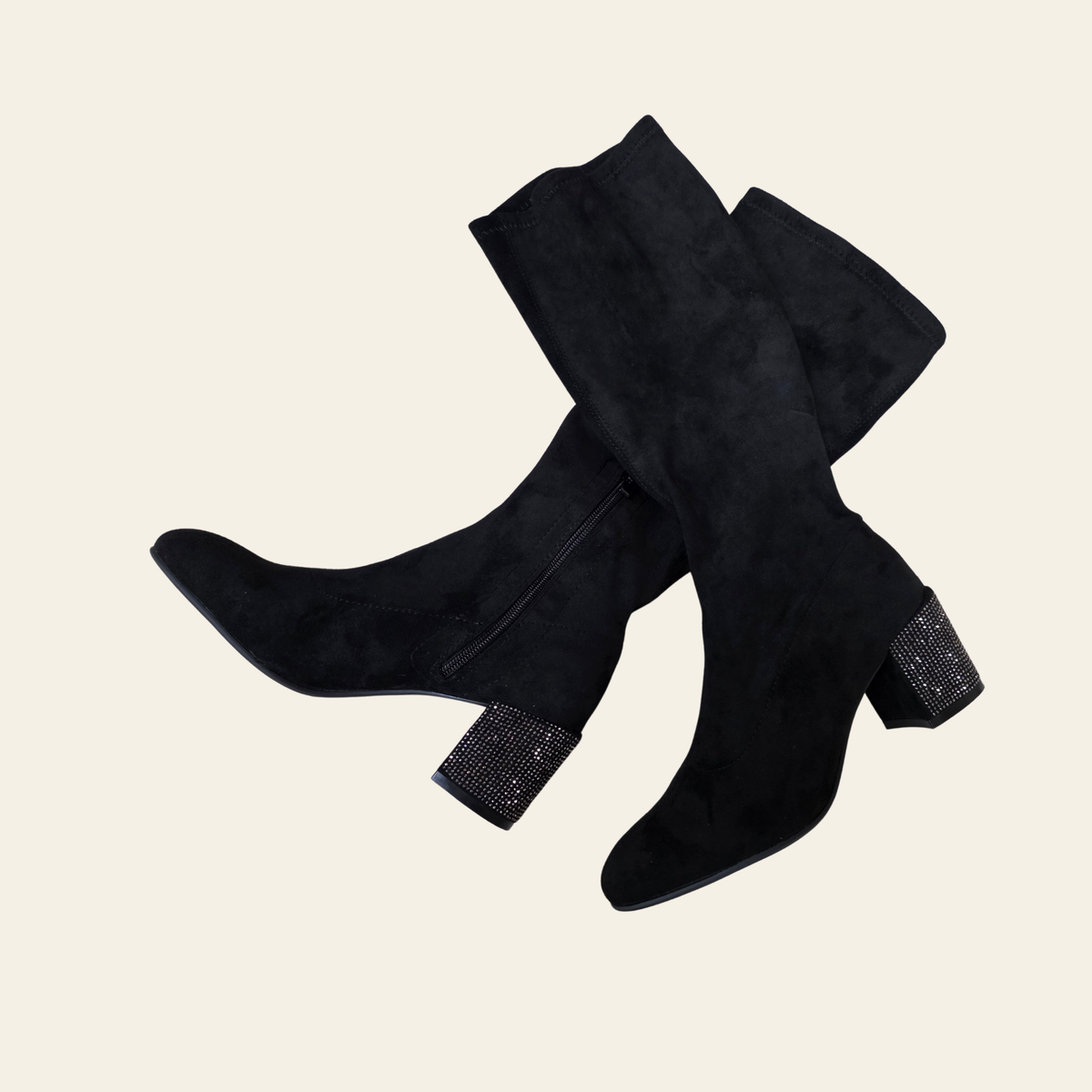 Black suede ankle boots with high stiletto heels, a platform sole, and a decorative rhinestone-embellished heels shown against a solid light beige background.