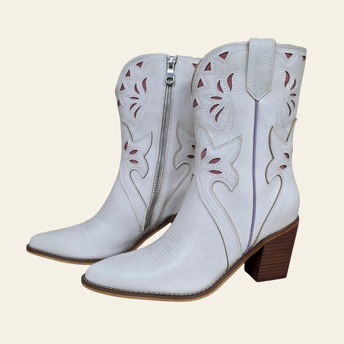 A pair of white western-style ankle boots with pointed toes, wooden block heels, and decorative cutout embroidery on the shafts, shown against a solid light beige background.