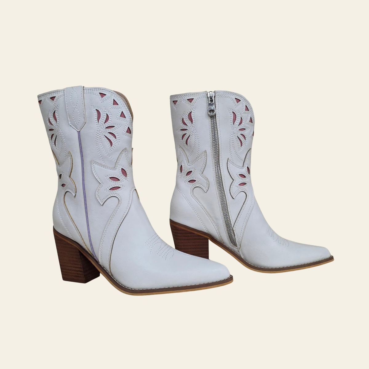 A pair of white western-style ankle boots with pointed toes, brown block heels, and decorative cutout embroidery on the shaft, shown against a solid light beige background.