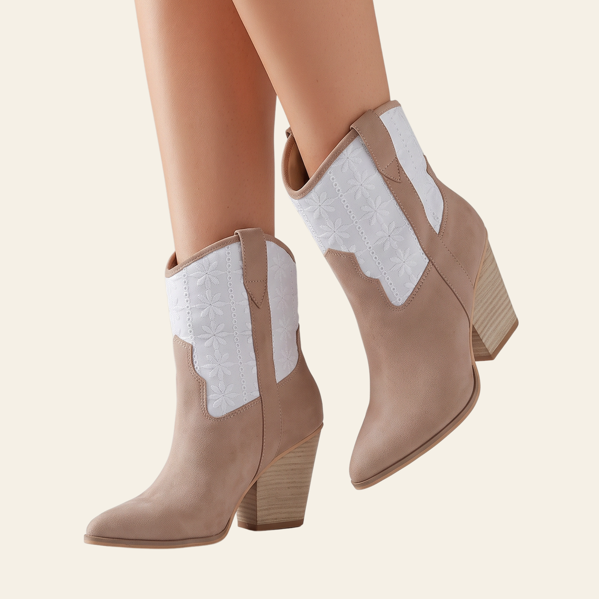 A pair of beige ankle boots with white western-style embroidered panels on the shaft, shown on a model's feet against a light cream background.