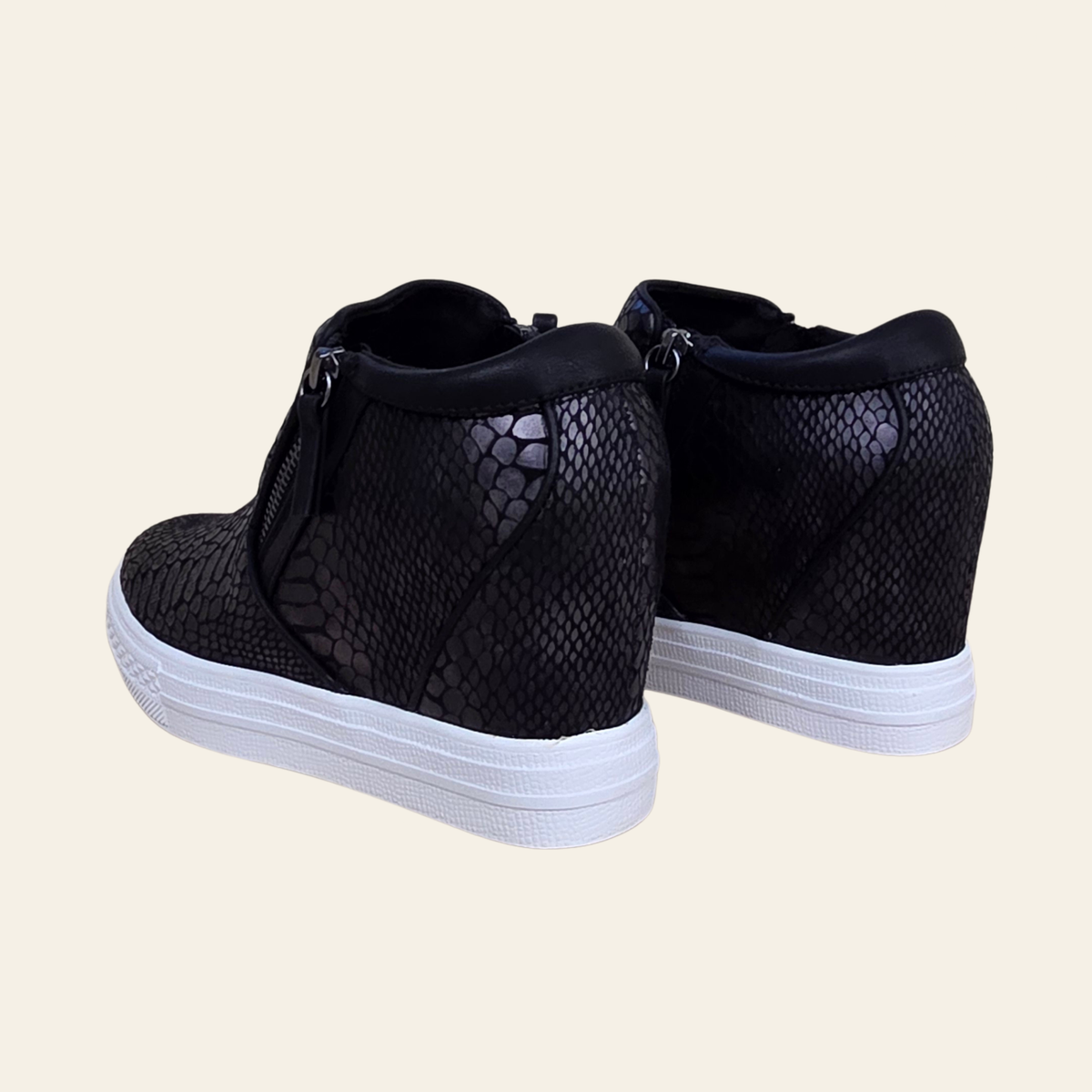 A pair of black high-top sneakers with a textured snakeskin pattern on the sides and white platform soles, shown from a three-quarters angle against a solid light beige background.