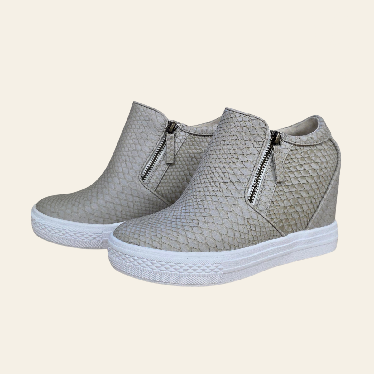 A pair of women's wedge ankle boots in a cream colored snakeskin pattern, featuring a side zipper and a thick white platform sole, set against a solid cream background.