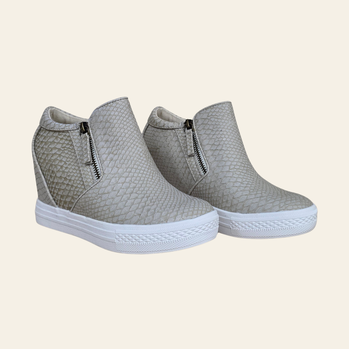 A pair of women's slip-on wedge sneakers with a textured, snakeskin-like pattern in cream, featuring side zippers and white platform soles, set against a solid cream background.