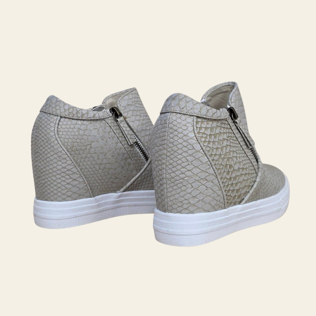 A pair of high-top sneakers with a textured snakeskin pattern in cream, featuring white platform soles and side zippers, shown against a solid cream background.