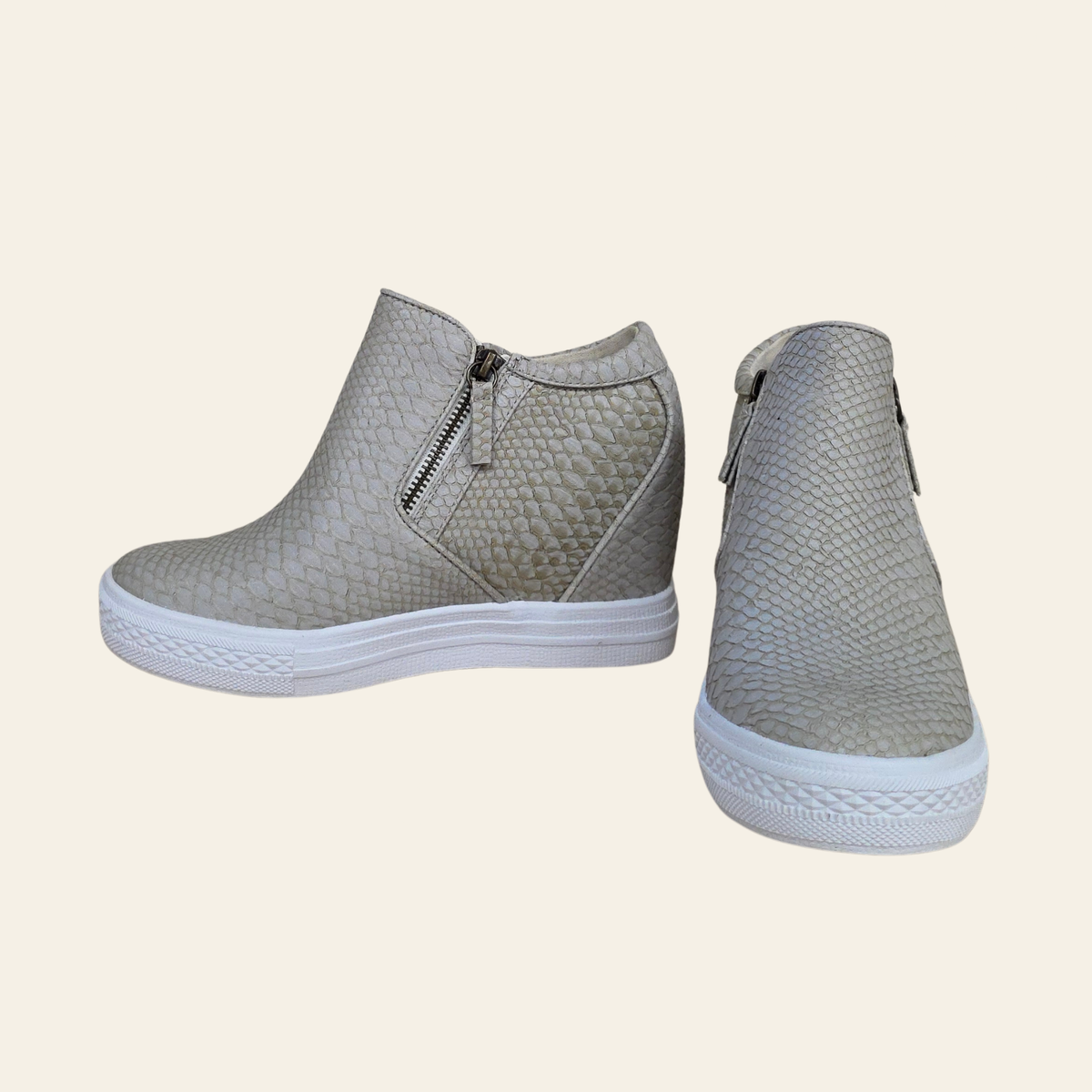 A pair of women's ankle boots with a textured, snakeskin-like pattern in cream, featuring side zippers and white platform soles, shown against a solid cream background.