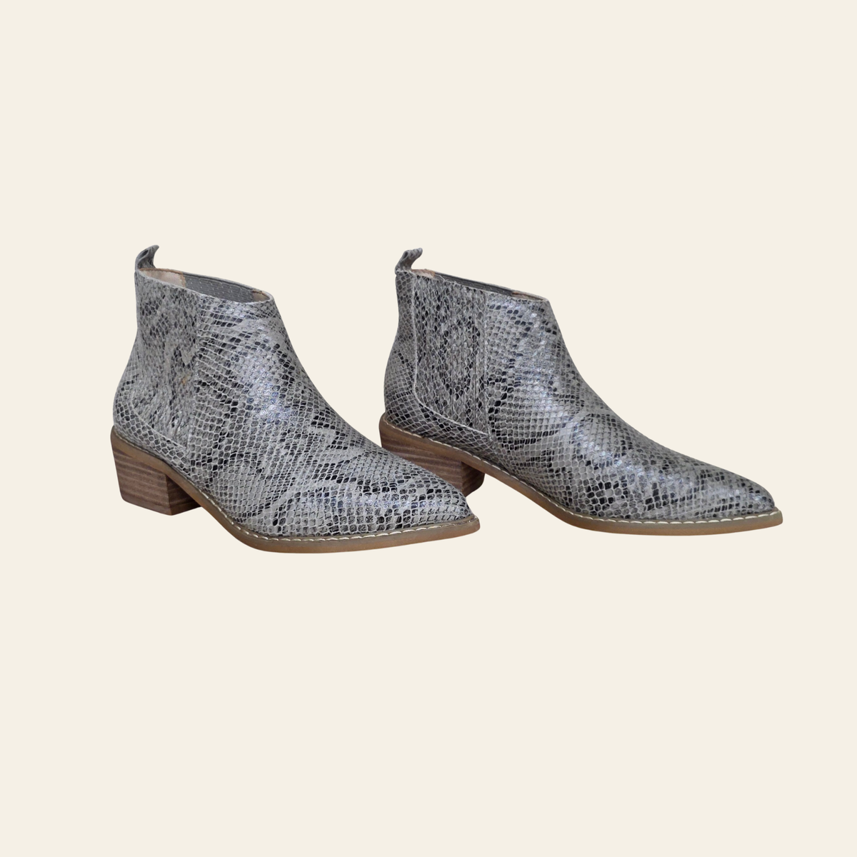 A pair of women's ankle boots featuring a gray and white snakeskin pattern with a low brown block heel, shown against a solid light beige background.