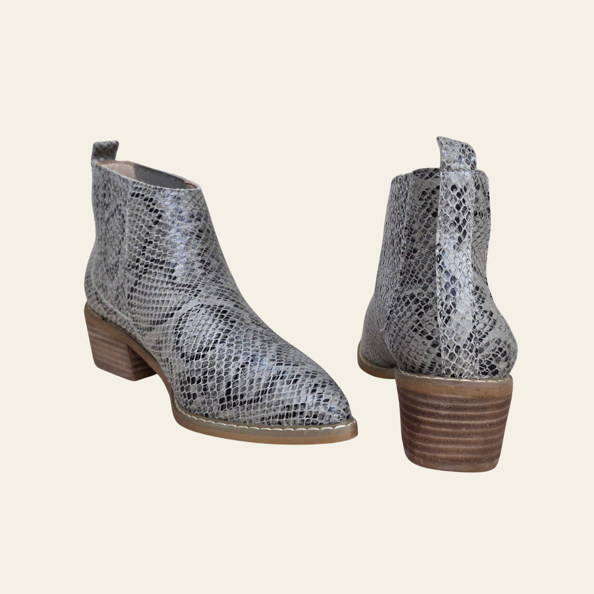 A pair of women's ankle boots featuring a gray and white snakeskin pattern, with a stacked brown wooden heel, shown from both front-three-quarter and side-back angles on a light cream background.