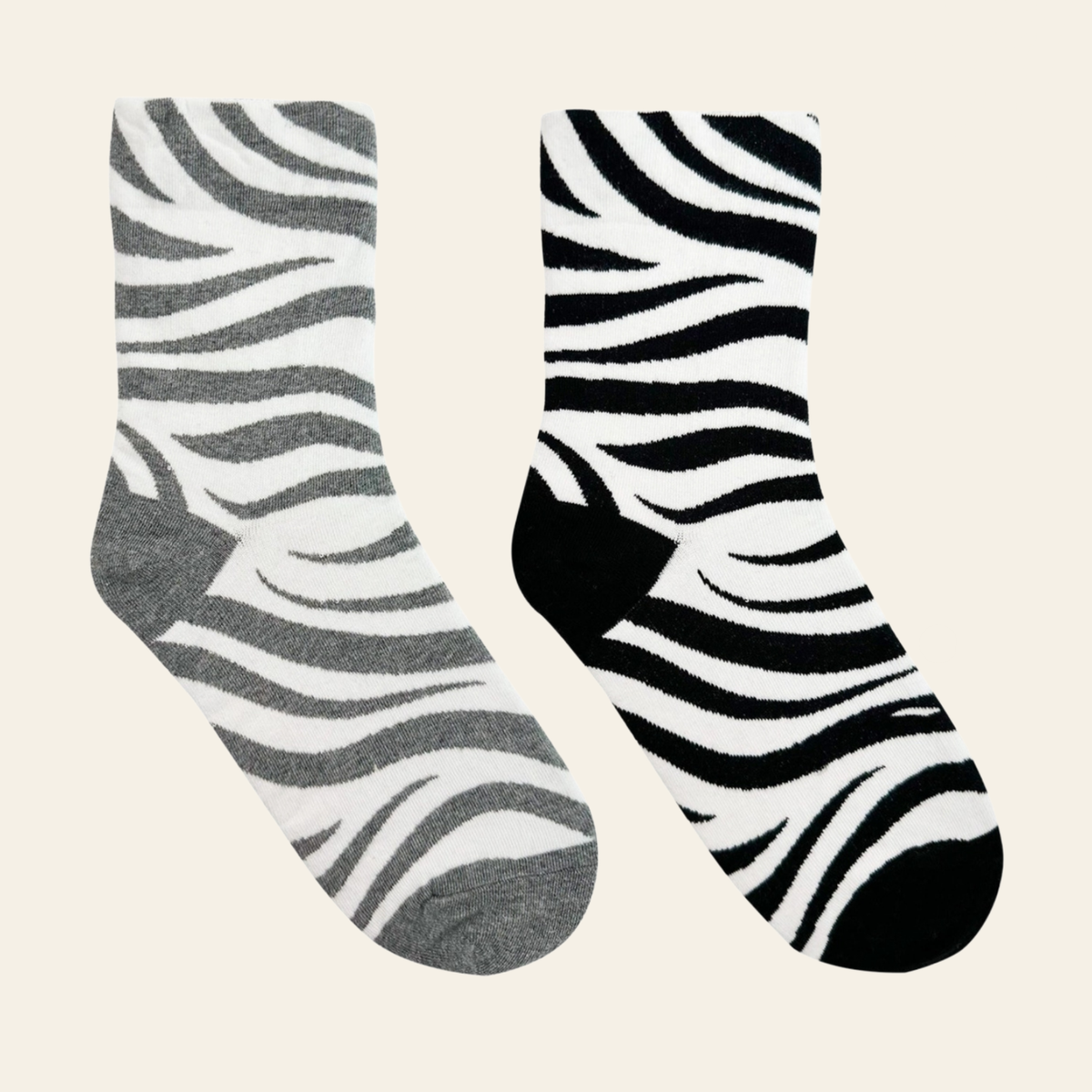 Two pairs of zebra-print socks on a light cream background. One pair is gray and white, and the other is black and white.