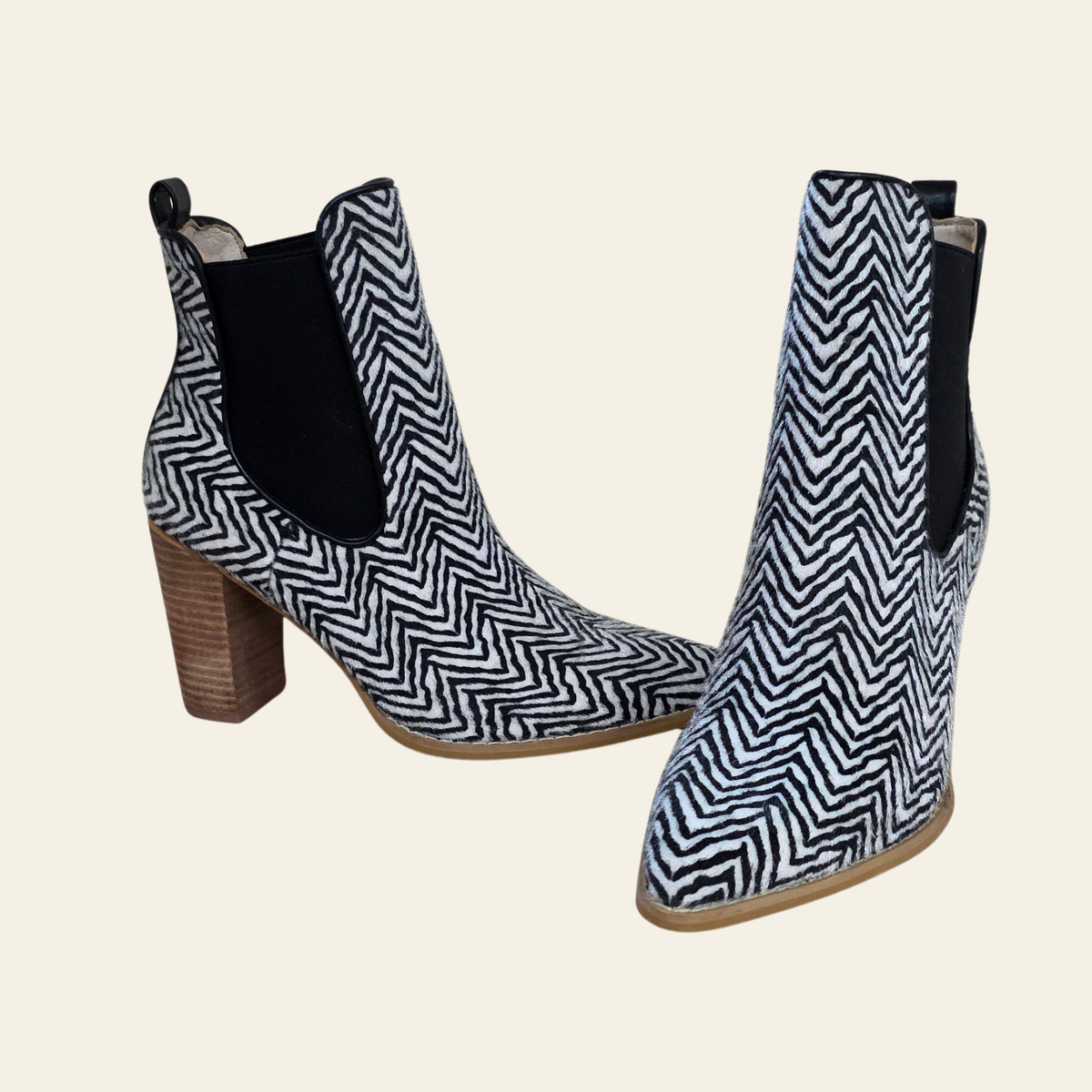 A pair of women's ankle boots with a black and white herringbone pattern, black elastic side panels, and a brown block heel, shown against a solid light beige background.