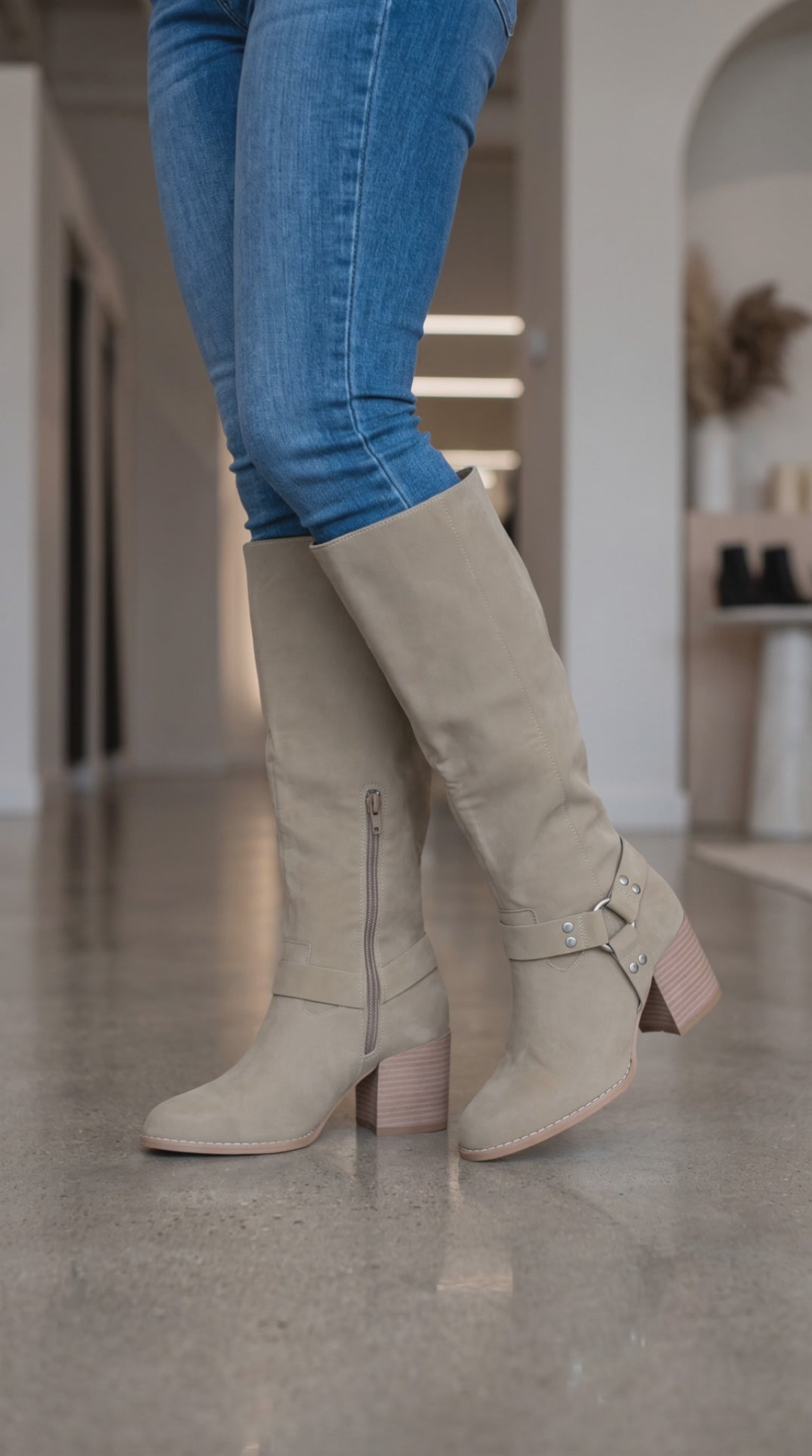 Model wearing taupe knee-high harness boots with silver stud accents and block heels, moving to show the boots from different angles.