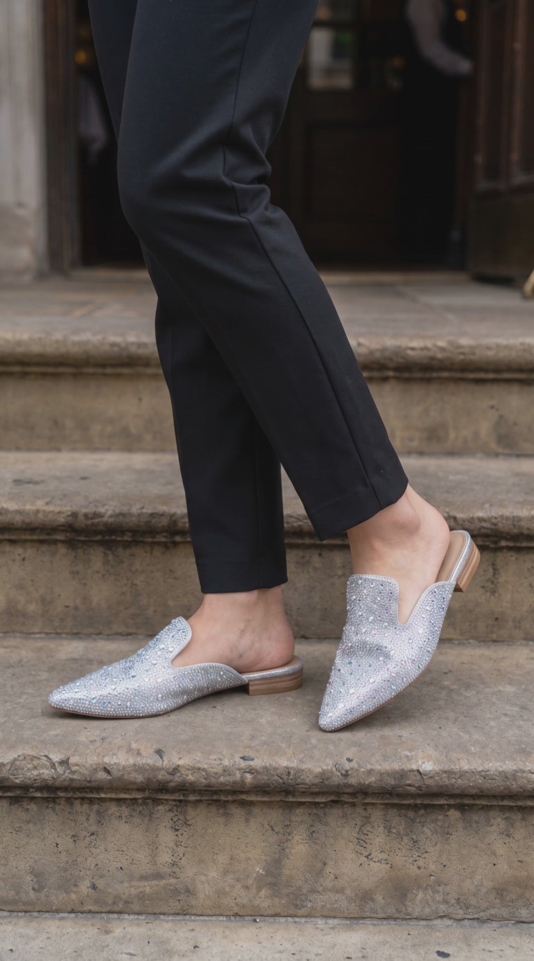 Plendino Gem rhinestone embellished mules on a model going down stairs.