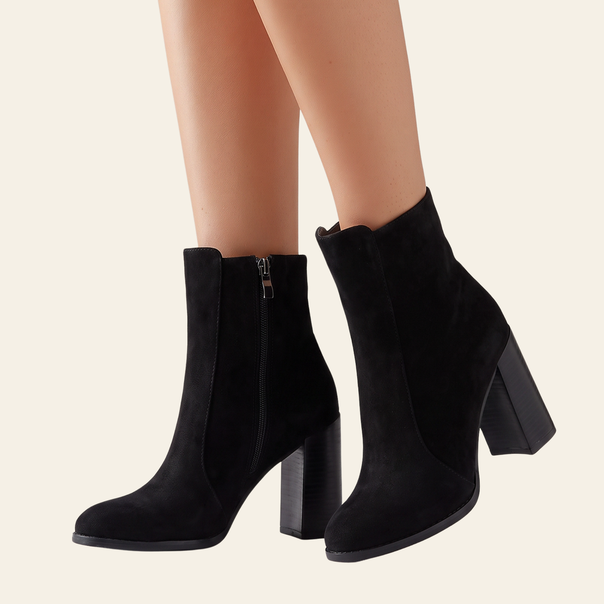 Black suede ankle boots with block heels and side zippers, shown on a model's feet against a light beige background.
