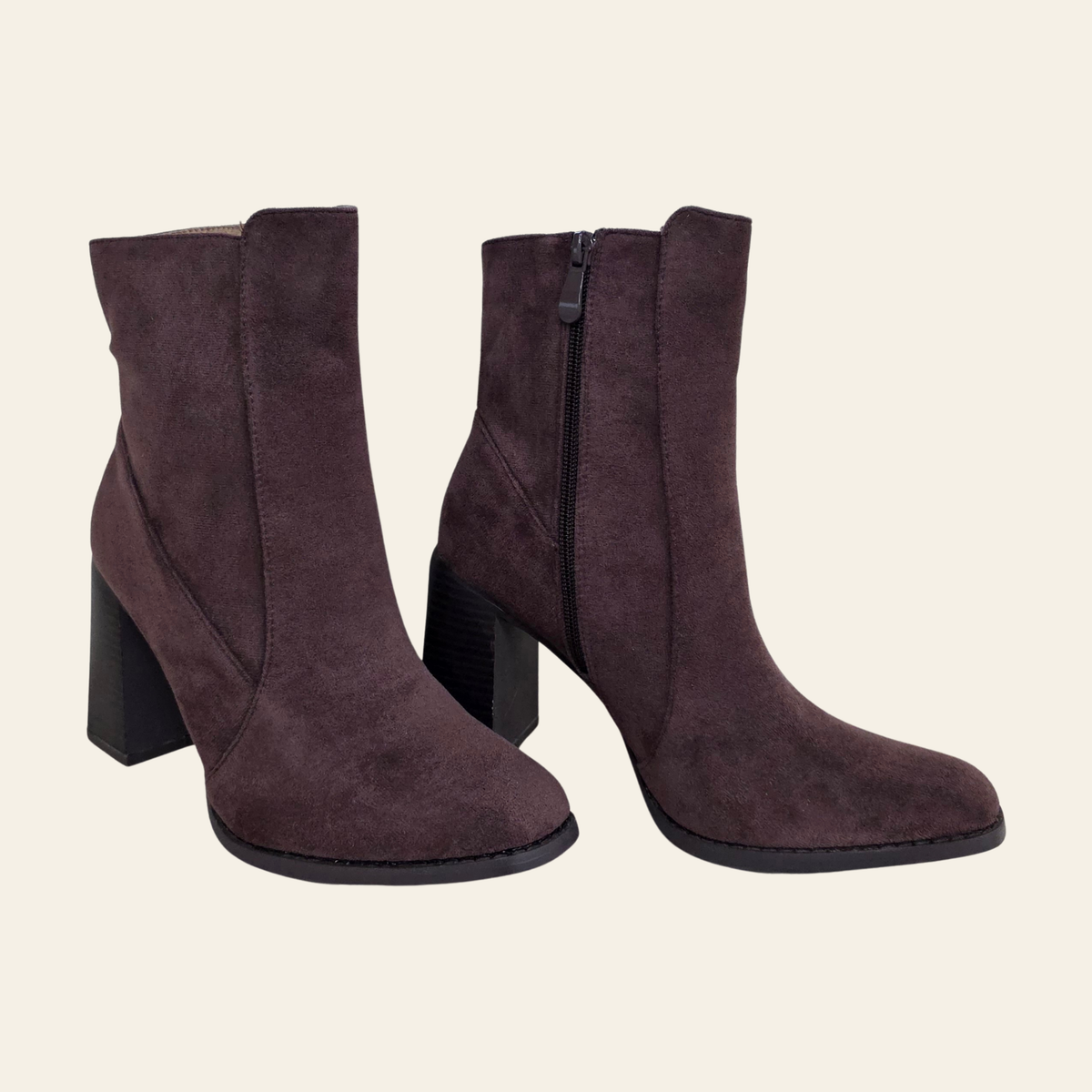 A pair of dark brown suede ankle boots with block heels and side zippers, shown against a solid off-white background.