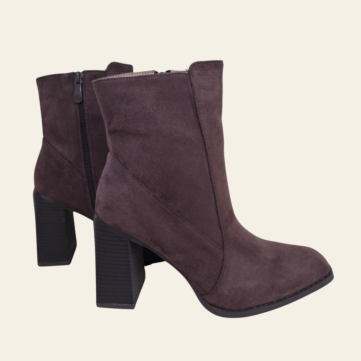 A pair of dark brown suede ankle boots with block heels and side zippers, shown against a solid light beige background.