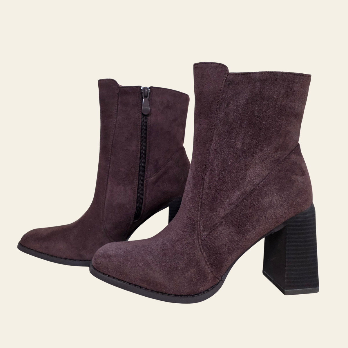 A pair of dark brown suede ankle boots with block heels and side zippers, shown against a solid light beige background.